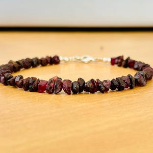May include: A red gemstone bracelet with a silver clasp. The bracelet is made of small, irregular shaped stones.