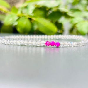 May include: A delicate bracelet made of small, clear beads with three bright pink beads in the center.