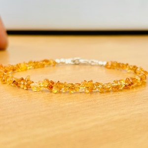 May include: A delicate gold-toned bracelet made of small, irregular-shaped gemstones. The bracelet is strung on a silver chain.