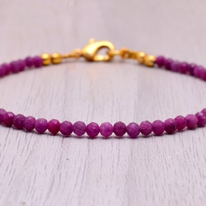 May include: A delicate bracelet made with small, faceted ruby beads and a gold clasp.