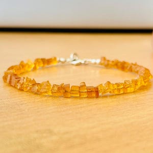Puede incluir: Un delicado brazalete hecho con pequeñas piedras de ámbar facetadas. El brazalete está enhebrado en una cadena de plata y tiene un cierre de plata.