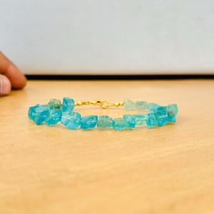 May include: A turquoise blue gemstone bracelet with gold accents. The bracelet is made of small, irregularly shaped stones.