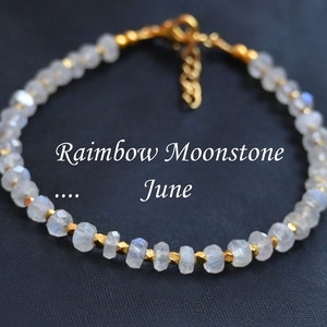 Op de afbeelding: Een gouden armband met witte regenboog-maansteen kralen. De armband heeft een gouden sluiting en is gemaakt met kleine gouden kralen tussen elke maansteen kraal. De tekst "Rainbow Moonstone... June" is zichtbaar in de afbeelding.