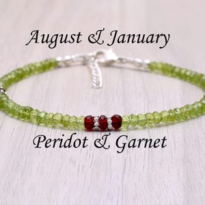 Könnte beinhalten: Ein zartes Armband aus grünen Peridot- und roten Granatperlen. Das Armband ist auf silbernem Draht gefädelt und hat einen silbernen Verschluss. Das Armband ist mit "August & January Peridot & Garnet" beschriftet.