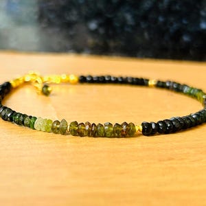 May include: A green and black gemstone bracelet with gold accents. The bracelet is made of small, round beads and has a simple design.