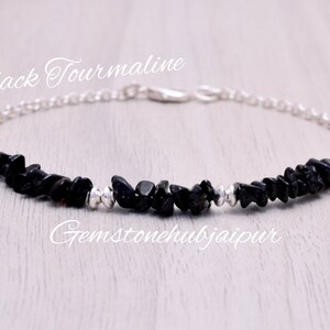 Puede incluir: Un brazalete de cadena de plata con virutas de turmalina negra. El brazalete está sobre una superficie de madera clara. El texto "Black Tourmaline" y "Gemstonehubjaipur" es visible en la imagen.