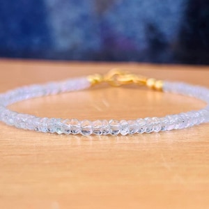 Könnte beinhalten: Ein zartes Armband aus winzigen, klaren Aquamarinperlen mit einem goldenen Verschluss.