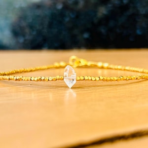 May include: A gold beaded bracelet with a clear quartz crystal charm.