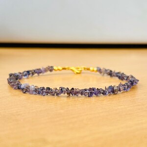 Può includere: Un braccialetto delicato realizzato con piccole pietre preziose irregolari di colore viola. Il braccialetto è infilato su una catena dorata con una chiusura.