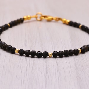 Peut inclure: Un bracelet en pierres précieuses noires avec des perles dorées et un fermoir doré.