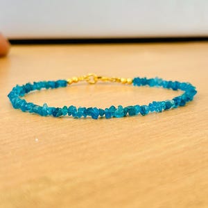 Könnte beinhalten: Ein zartes blaues Edelstein-Armband mit einem goldenen Verschluss. Das Armband besteht aus kleinen, unregelmäßig geformten Steinen.