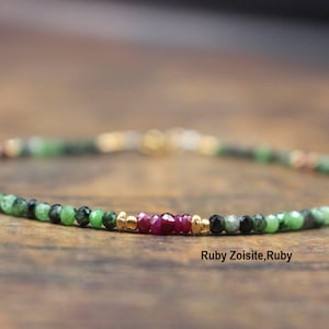 May include: A delicate bracelet made with green zoisite, ruby, and gold beads. The bracelet is on a wooden surface. Ruby Zoisite, Ruby