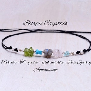 May include: A black string bracelet with silver beads and five different colored gemstones: peridot, turquoise, labradorite, rose quartz, and aquamarine. The bracelet is labeled "Scorpio Crystals".