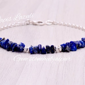 Puede incluir: Un brazalete de cadena de plata con una fila de chips de lapislázuli azul oscuro. El brazalete tiene un cierre de broche. El texto "Lapis Lazuli" está escrito sobre el brazalete y "Gemstonehubjaipur" está escrito debajo del brazalete.