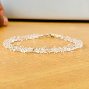 Può includere: Un braccialetto delicato fatto di piccole pietre di quarzo trasparenti. Il braccialetto è infilato su una sottile catena d'argento.