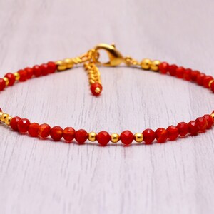 Pode incluir: Uma pulseira delicada com pequenas contas vermelhas facetadas. Contas douradas e um fecho dourado adicionam contraste. A corrente ajustável permite um ajuste confortável. Uma peça de joalharia simples, mas elegante.