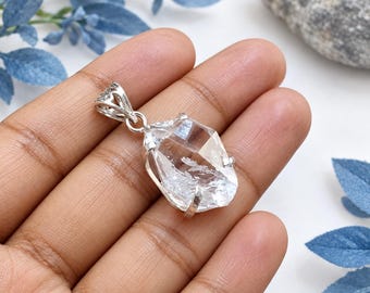 Può includere: Un ciondolo in cristallo di quarzo trasparente sfaccettato montato su una montatura in metallo argentato con griffe. Il ciondolo presenta un gancio triangolare sulla parte superiore, che mette in risalto la forma naturale della pietra.