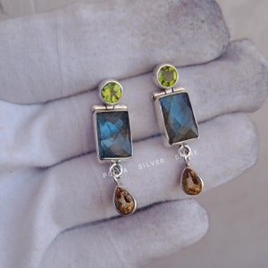Puede incluir: Pendientes de plata de ley con una piedra preciosa de labradorita cuadrada, una piedra preciosa verde más pequeña y una piedra preciosa marrón en forma de lágrima.