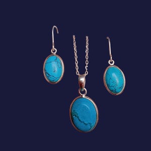 May include: A silver necklace and earrings set featuring oval turquoise stones. The necklace has a delicate chain and a pendant with a turquoise stone. The earrings are drop earrings with turquoise stones.