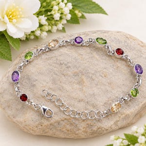 Può includere: Un bracciale a catena color argento con diverse pietre preziose dal taglio ovale in vari colori, tra cui viola, verde, rosso e giallo. Il bracciale include una chiusura a moschettone e una catenella di estensione regolabile con maglie circolari.
