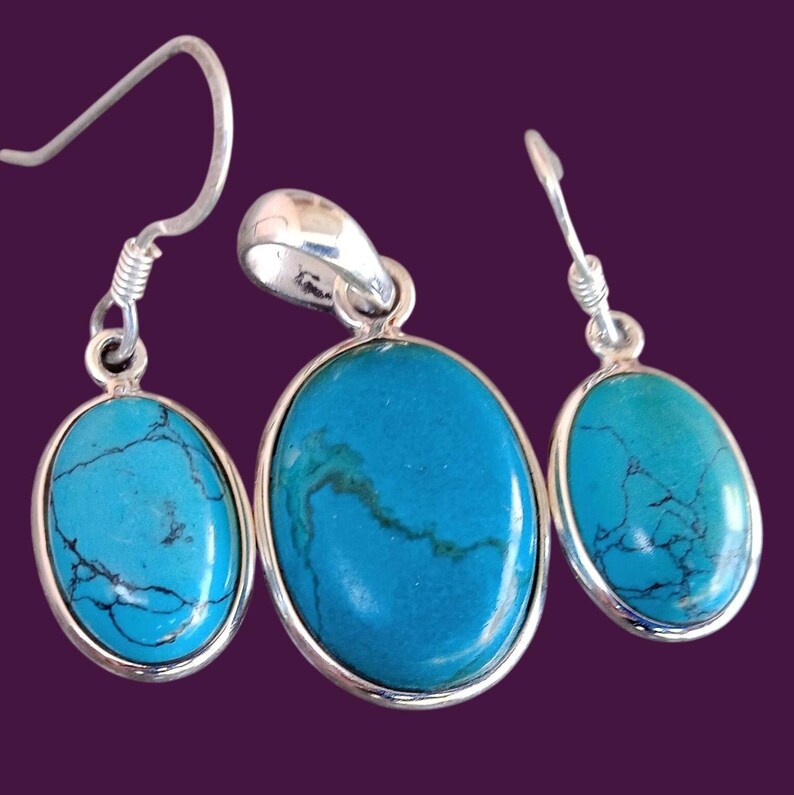 May include: A turquoise gemstone pendant and earrings set with silver accents. The oval-shaped stones have a blue-green colour with dark veins.