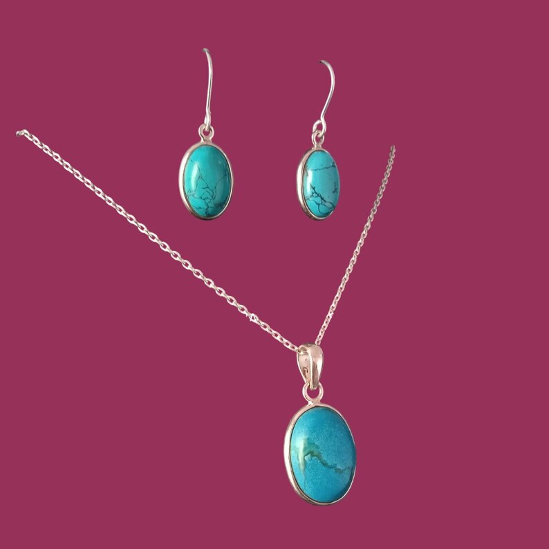 May include: A silver necklace and earrings set with oval turquoise stones. The necklace has a delicate chain and a pendant with a turquoise stone. The earrings are drop earrings with turquoise stones.