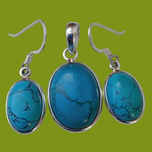 May include: A set of silver earrings and a pendant featuring oval-shaped turquoise stones. The stones have a blue-green colour with dark veins running through them.