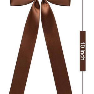 May include: A brown satin bow tie, 5 inches wide and 10 inches long, with long, flowing tails. The bow is a solid, rich brown color, suitable for formal or casual wear. The bow tie is a classic accessory.