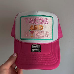 May include: Pink trucker hat with a white front panel featuring an embroidered patch that says "TACOS AND MARGS" in pink, orange, and green lettering with a margarita glass graphic. The hat has a black "OTTO WORLD FAMOUS FOAM FRONT" label.