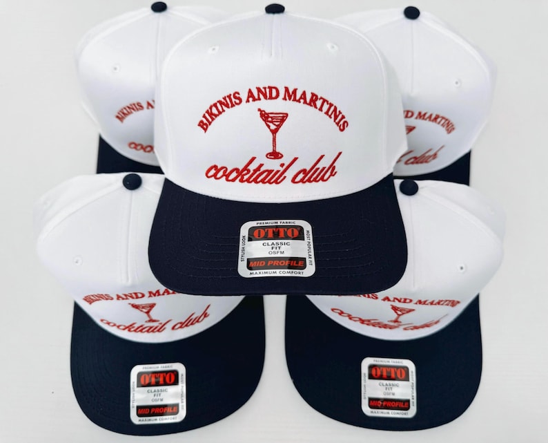 May include: Five white and navy blue baseball caps with the text "Bikinis and Martinis cocktail club" in red and white lettering. Each cap has a red martini glass graphic and a black and white label with the text "OTTO" in white.