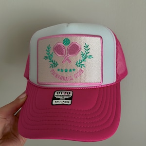 May include: Pink and white trucker hat with a pink and green embroidered patch that says "Pickleball Club" with a pickleball and paddles inside the patch. The hat has a black label that says "OTTO World Famous Foam Front OSFA TRUCKER".