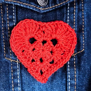 Puede incluir: Un corazón rojo tejido a crochet sobre un fondo de mezclilla azul.