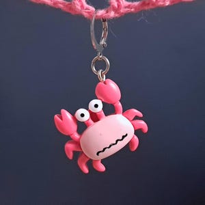 Pode incluir: Um chaveiro de plástico rosa em forma de caranguejo com olhos saltitantes. O caranguejo está preso a um chaveiro prateado.