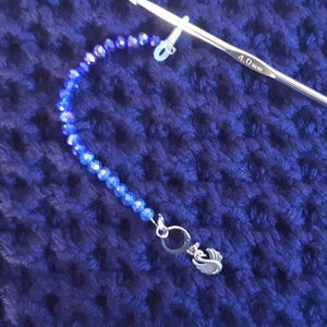 May include: A blue and clear crystal bead chain with a silver swan charm attached to a 4.0 mm crochet hook.