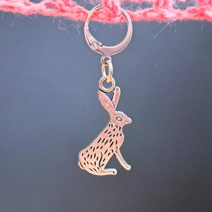 May include: A silver charm in the shape of a rabbit, hanging from a silver ring. The rabbit is sitting with its ears up and its tail behind it.