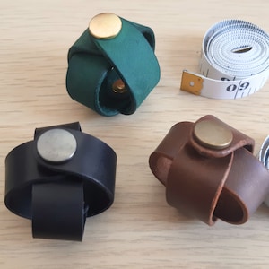 May include: Three leather bracelets with metal clasps. The bracelets are green, brown, and black. The bracelets are on a wooden surface.