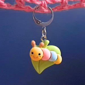 May include: A silver charm featuring a green leaf and a yellow and pink caterpillar with blue and orange accents.