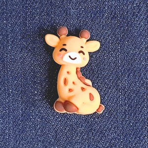 May include: A small, yellow giraffe figurine with brown spots and a smiling face. The figurine is made of a soft, pliable material and is ideal for adding a touch of whimsy to any craft project.
