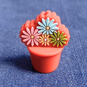May include: A small red flower pot with four colorful flowers on top. The flowers are pink, blue, green, and yellow.