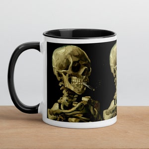 May include: White ceramic mug with a black rim and handle. The mug features a colorful image of a skeleton smoking a cigarette. The image is a stylized interpretation of a famous painting.