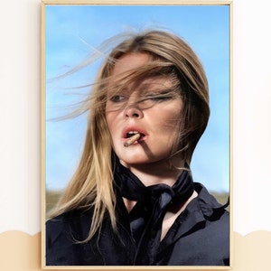 May include: A woman with long blonde hair is wearing a black shirt and a black scarf. Her hair is blowing in the wind and she is holding a cigarette in her mouth. The background is a blue sky.