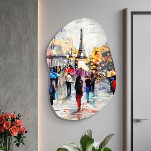 May include: A colorful abstract painting of people walking under umbrellas in front of the Eiffel Tower in Paris, France. The painting is on a white background with a textured, irregular shape.