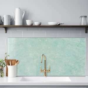 May include: A kitchen sink with a gold faucet and a light blue glass backsplash. The backsplash has a marbled effect.