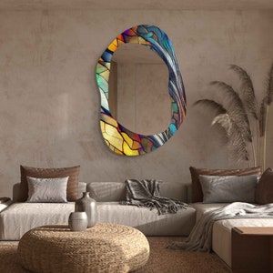 May include: A large, abstract, colorful, oval-shaped mirror with a stained glass design. The mirror is hanging on a beige wall in a living room setting.