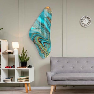 May include: Abstract wall art featuring a teal, gold, and black marbled design. The art is shaped like a teardrop and is mounted on a white wall.