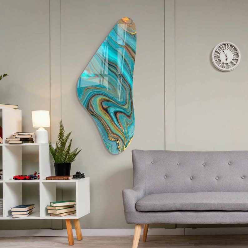 May include: Abstract wall art featuring a teal, gold, and black marbled design. The art is shaped like a teardrop and is mounted on a white wall.