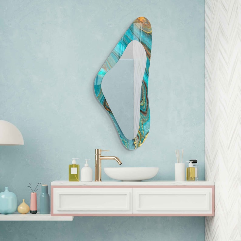 May include: A bathroom vanity with a white countertop and two drawers. A gold faucet and a white oval sink are on the countertop. A blue and gold abstract mirror hangs on the wall above the sink.