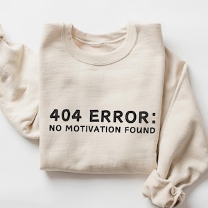 May include: A beige sweatshirt with the text "404 ERROR: NO MOTIVATION FOUND" printed in black.