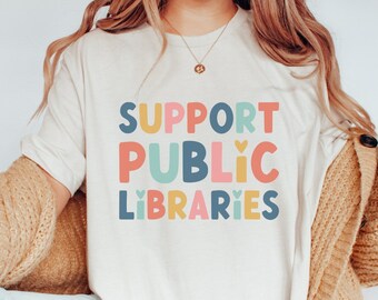 May include: A white t-shirt with the text "SUPPORT PUBLIC LIBRARIES" in colorful letters. The letters are outlined in black and have a heart shape in the middle of each letter.