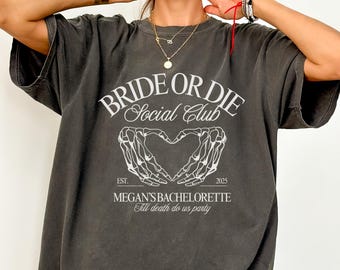May include: An oversized t-shirt in a dark grey colour with the text "Bride or Die Social Club" and a skeleton hand heart graphic. The text "Est. 2025" and "Megan's Bachelorette 'Till death do us party'" are also printed on the shirt.